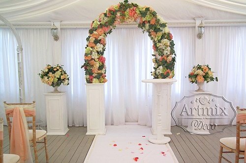 Полукруглая свадебная арка из цветов на фоне белых тумб