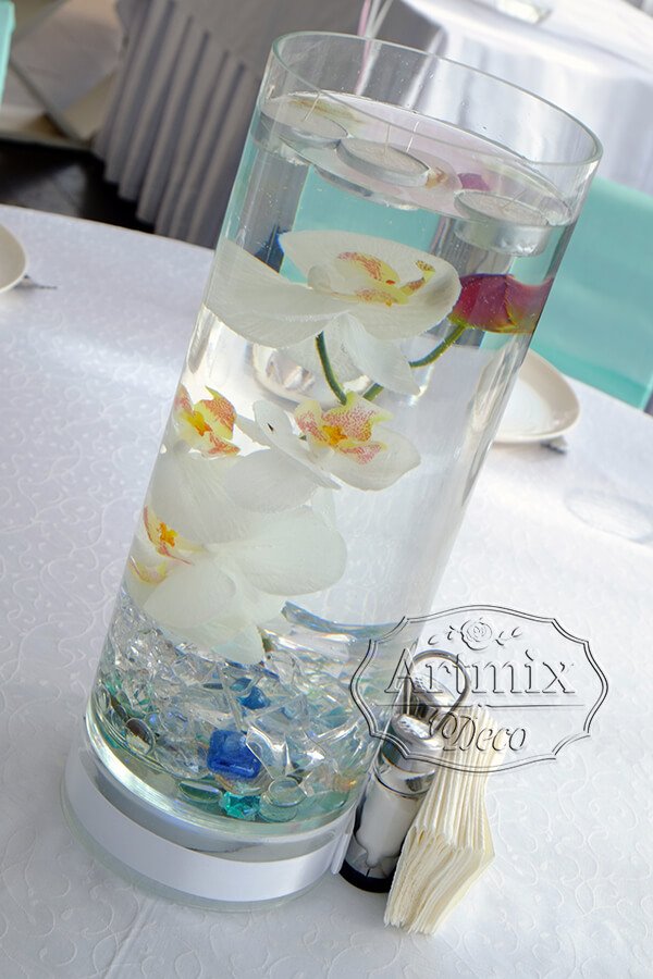 Орхидеи в прозрачной вазе, украшаются стеклянными камешками и подсвечивается светодиодной подсветкой и наверх помещаются плавающие свечи