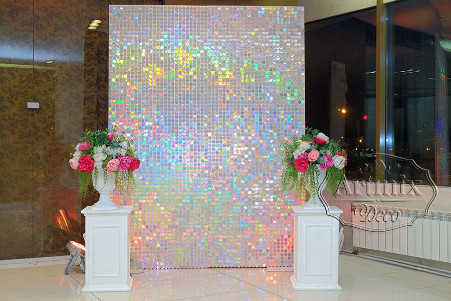 Фотозона из перламутровых пайеток с декоративными напольными колоннами и яркие цветочными композициями