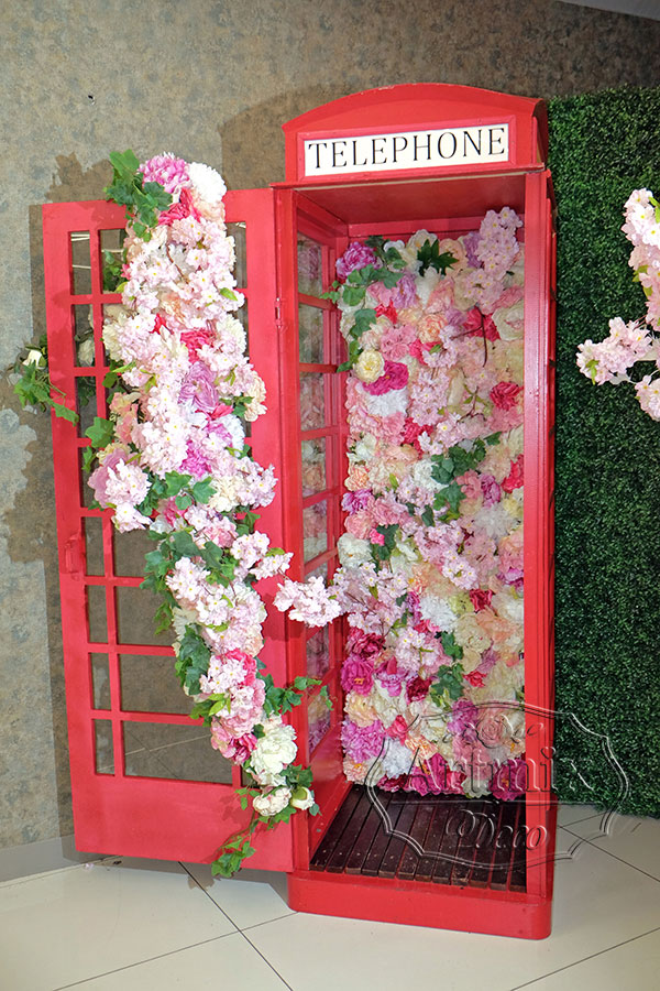 Фотозона "Телефонная будка" с цветами и бело-розовым деревом на фоне стены из самшита