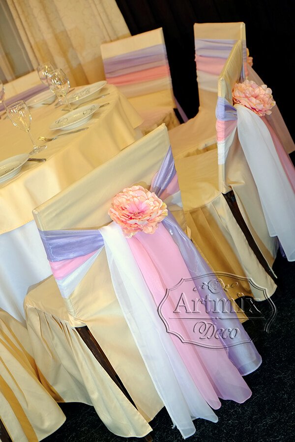 Белые, розовые и сиреневые ленты в оформлении стульев для свадебного торжества