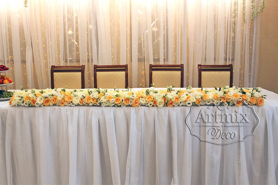 На столе жениха и невесты гирлянда из живых цветов или цветочная композиция из роз вытянутой форму