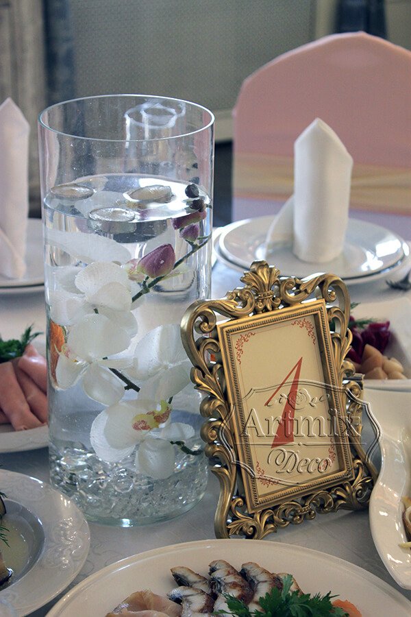 Оригинальные композиции на столах гостей, где цилиндрические вазы наполнены водой и погруженные в них орхидеи с плавающими свечами