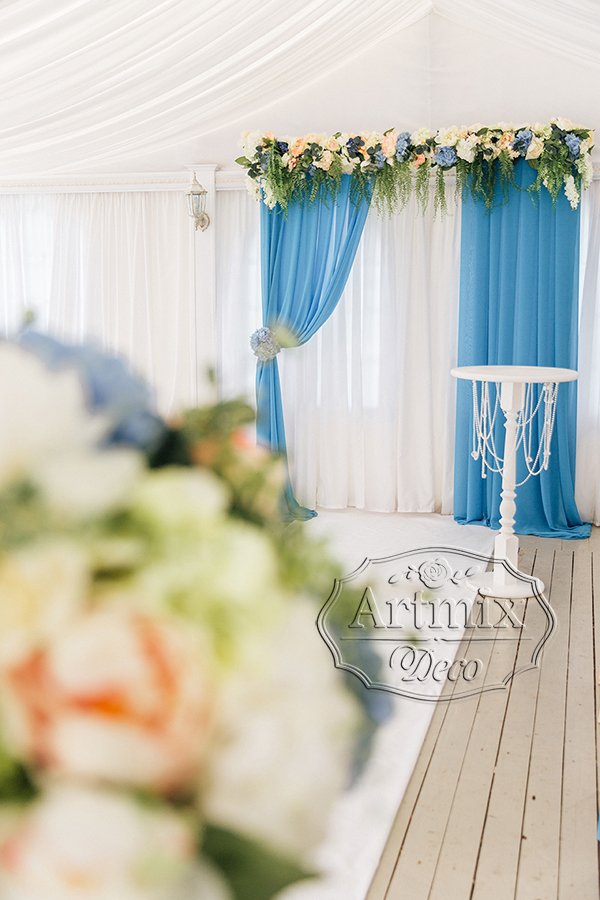 Свадебная арка украшена гирляндой из цветов и текстилем голубого цвета