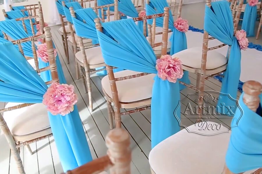 Голубые ленты и нежные цветы розового цвета в оформлении стульев